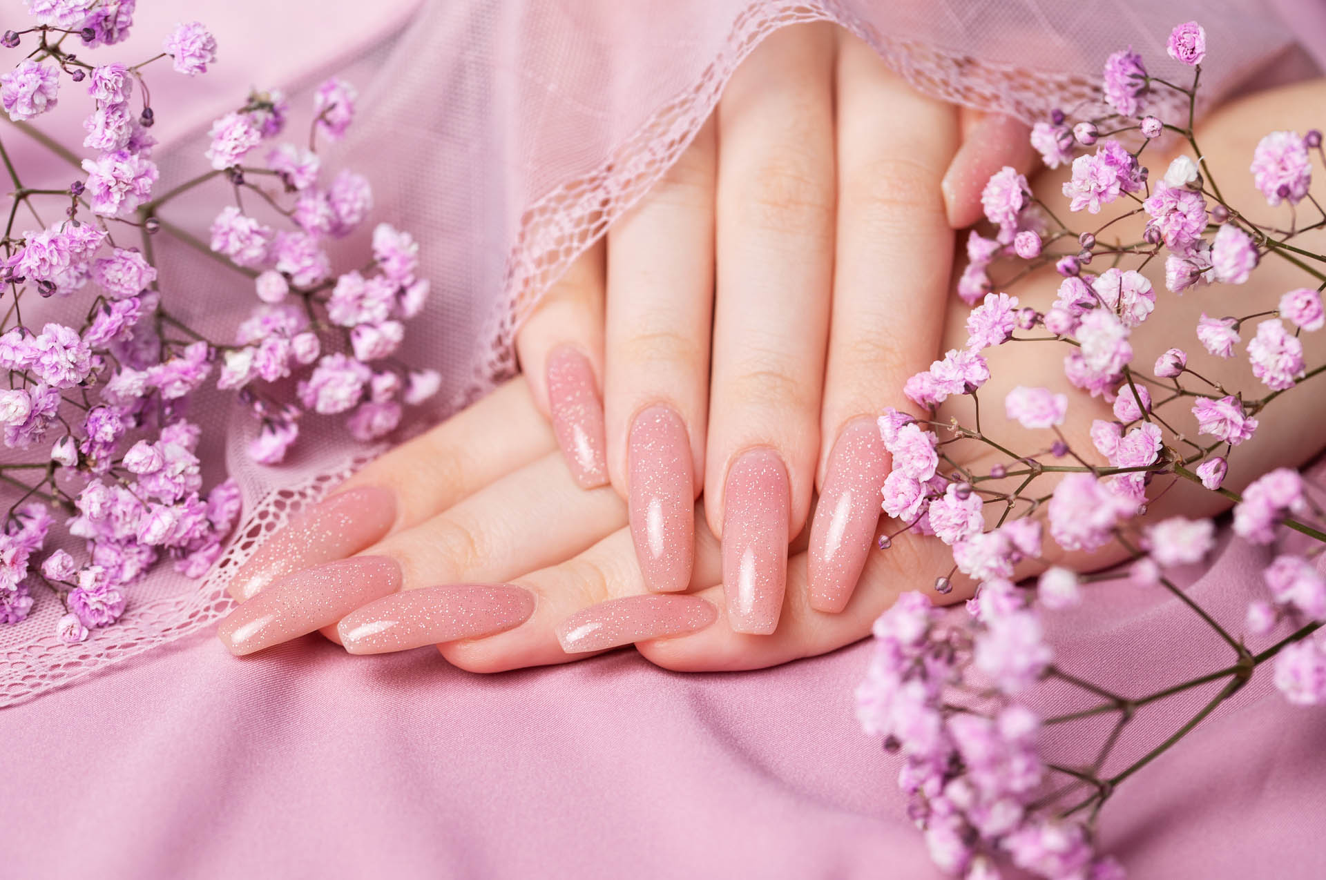 Female hands with pink nail design  hold gypsophila flowers. Pink nail polish manicure on pink background